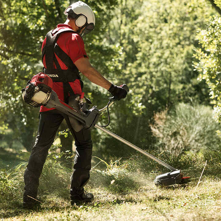 Uomo che usa il decespugliatore con un casco bianco
