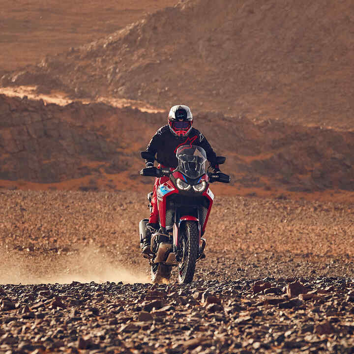 Modello alla guida di una moto CRF1100L Africa Twin in un luogo desertico.